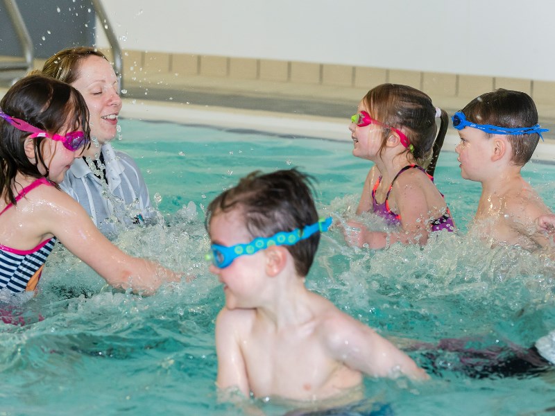 A group of young children splashing about in the pool