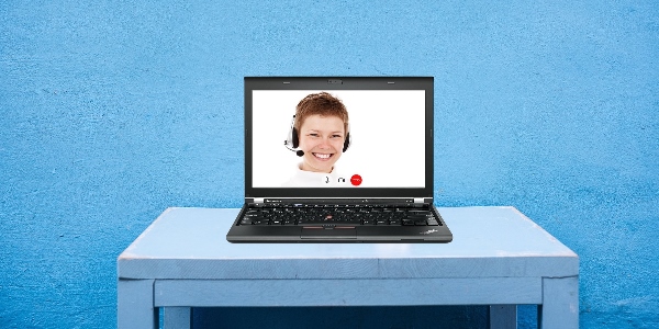 A laptop sitting on a table with a person on the screen ready to help