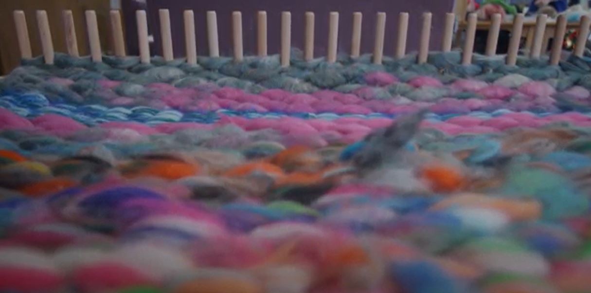 colourful wool fibres in foreground with weaving equipment in background