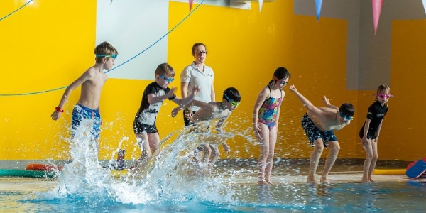 A group of children jumping into the pool as part of a swim lesson